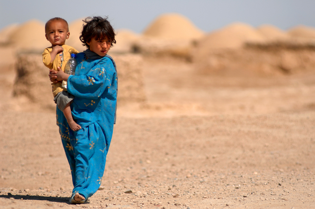 Morgan Kacha village, Southern Afghanistan. A young Afghan girl carries her younger brother as she makes her way to the school house, March 31, 2010. U.S. Army and Afghan National Army soldiers visited the village to deliver school supplies for children. U.S. forces, currently present in Afghanistan, support the Afghan National Security Forces in counterinsurgent operations. U.S. Air Force. Senior Airman Kenny Holston.