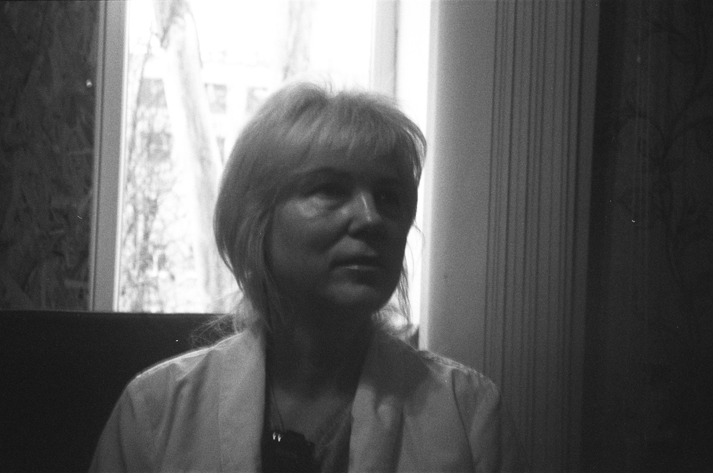 Ніна Александрова, директор центру первинної медико-санітарної допомоги в Петропавлівці Дніпропетровської області, сидить перед вікнами, закритими OSB-плитами; на тлі видно пошкоджену лікарню.<br>Фото: Pat Griffiths/ICRC