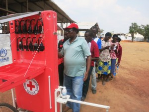 מאהאמה, רואנדה. מוטבים עומדים בתור מאחורי איש סגל של ה-ICRC לשירות הטעינה החינמי של טלפונים ניידים.  CC BY-NC-ND / ICRC / Emmanuel Kagimbura 